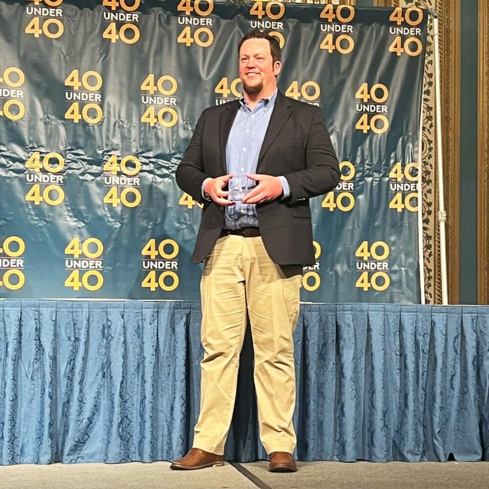 A man standing on stage holding an award for being a 40 Under 40 Star.