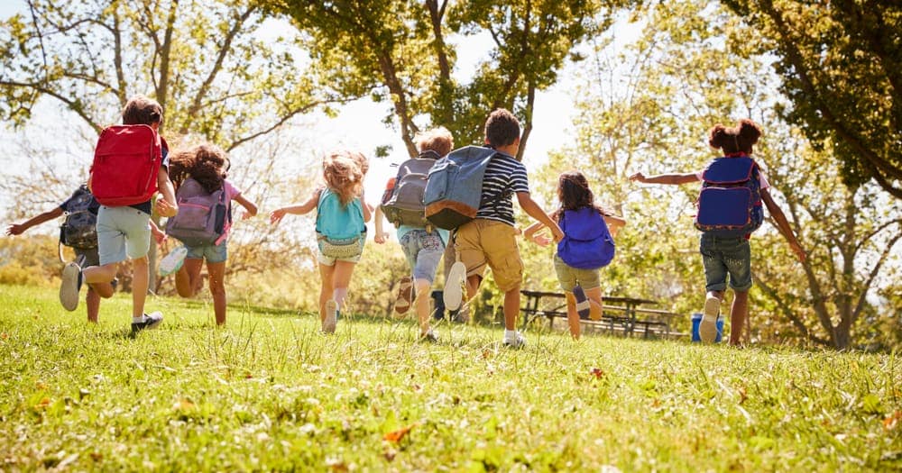A group of children running with backpacks on the grassy field at Bay City State Park.