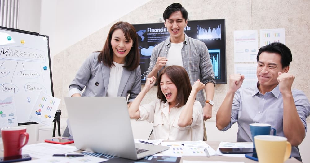 A group of Asian business people are laughing in front of a laptop, showcasing their 
Presence as they gather around the Blue Compass RV in North Carolina.