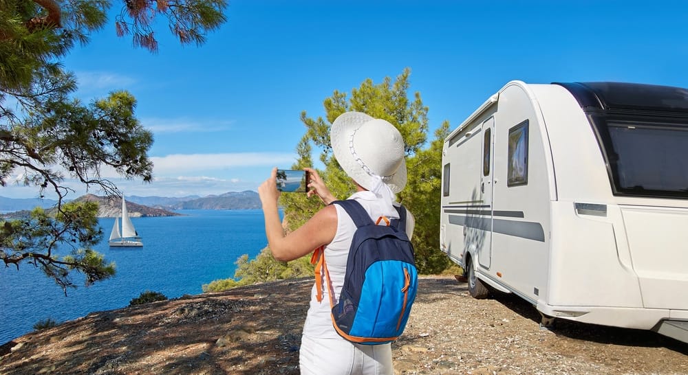 A woman is capturing the scenic view of her RV with the ocean in the background during Snowbird Travel.