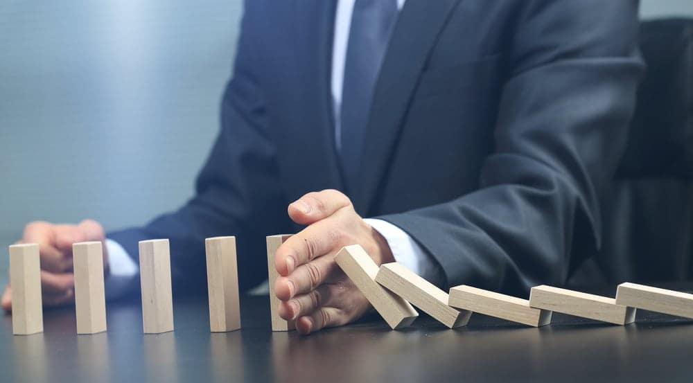 A businessman in a suit is putting dominoes on a table as part of a proposal.