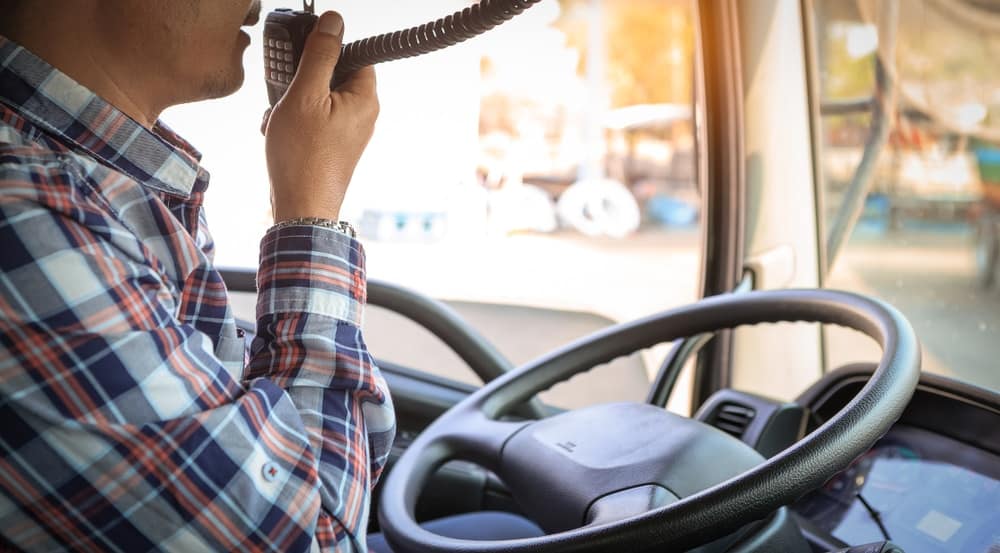 A man is driving a truck equipped with the Ultra-Compact CB Radio from Cobra Electronics, while talking on the phone.