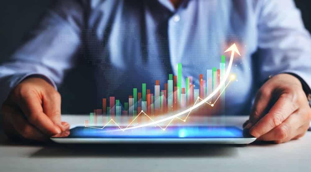 A man is holding a tablet displaying a graph illustrating growth reports.