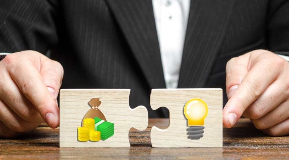 A businessman holding a puzzle piece with money and a light bulb, showcasing his innovative approach to financial problem-solving.