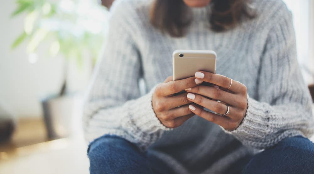 A woman sitting on the floor holding a cell phone, enjoying CampON downloads during Camping Season.