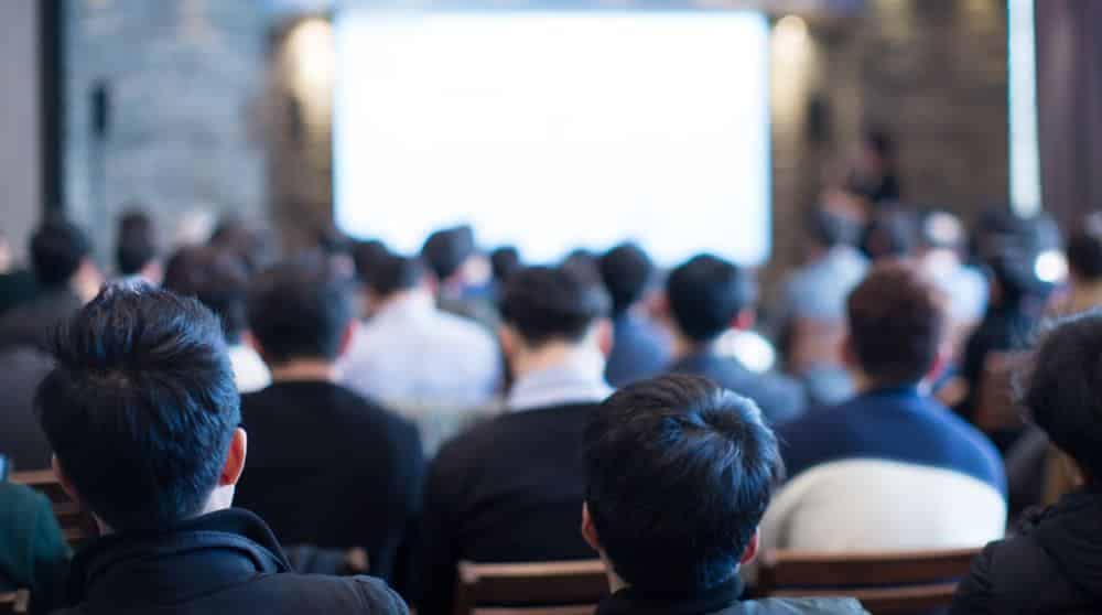 A group of people at the CampCalNOW Summit in an auditorium, watching a presentation on Park Rules by Rudderow Law Group.