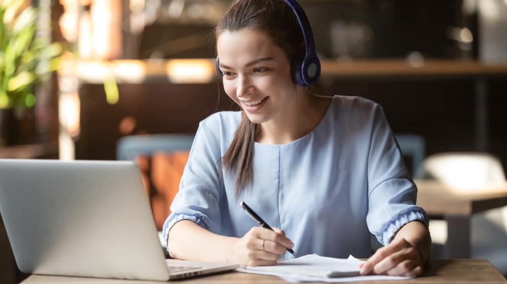 A woman wearing headphones is working on a laptop in a cafe during a Zoom session with BCLCA directors.