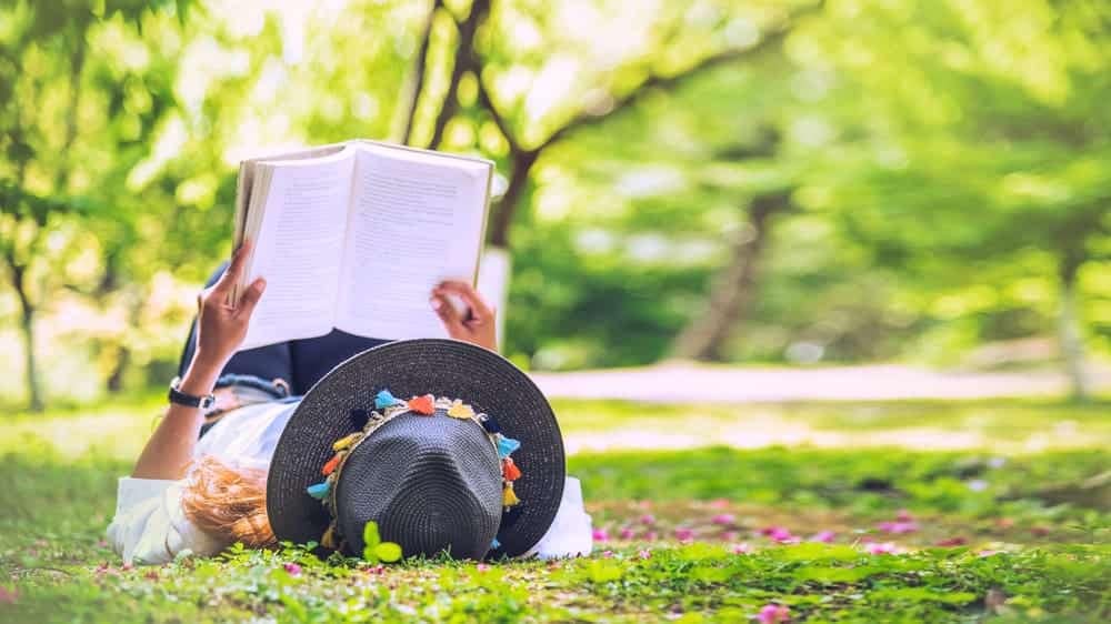 A woman relaxing on the grass, engrossed in a captivating book at a Kansas State Park.