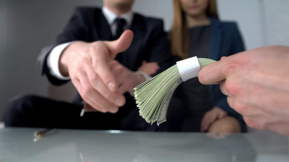A businessman is handing money to a woman in a business meeting.