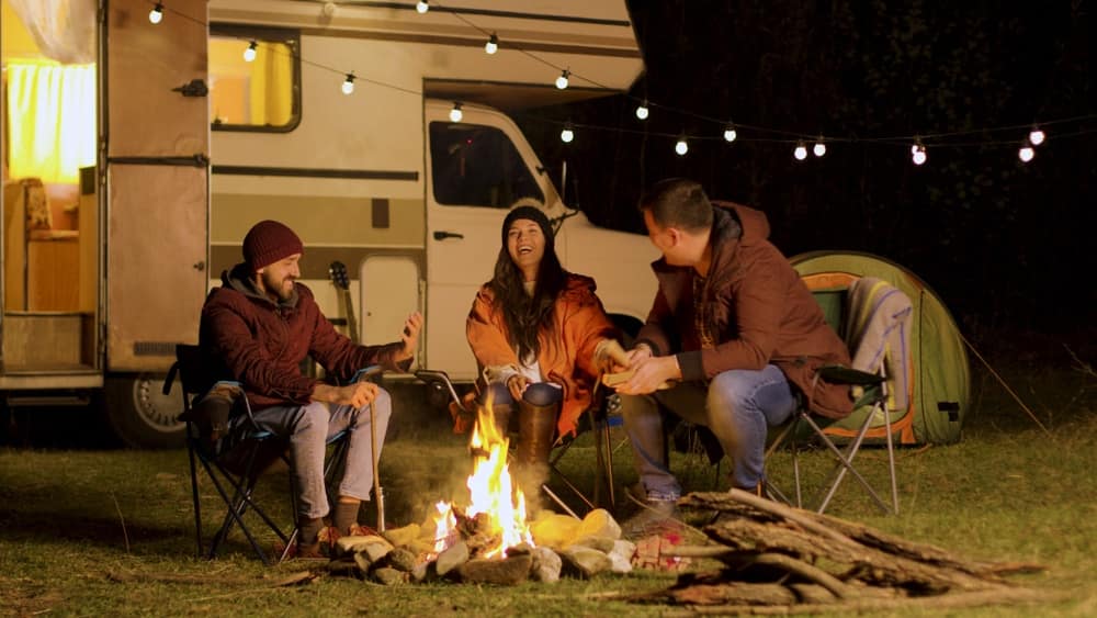 Three Australians sitting around a campfire in front of an RV in the bush.