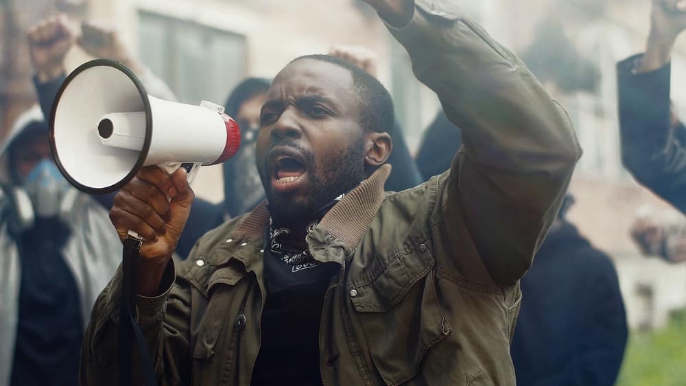 A man shouting into a megaphone at a counterprotesters gathering during a block party, trying to deter their activities.