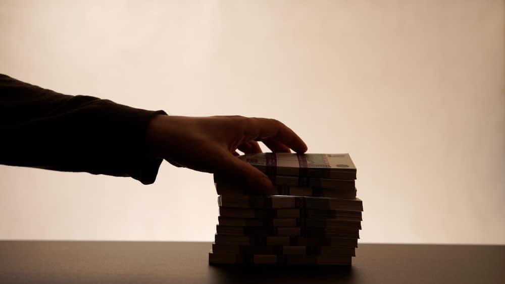 An employee's hand holding a stack of money on a table.