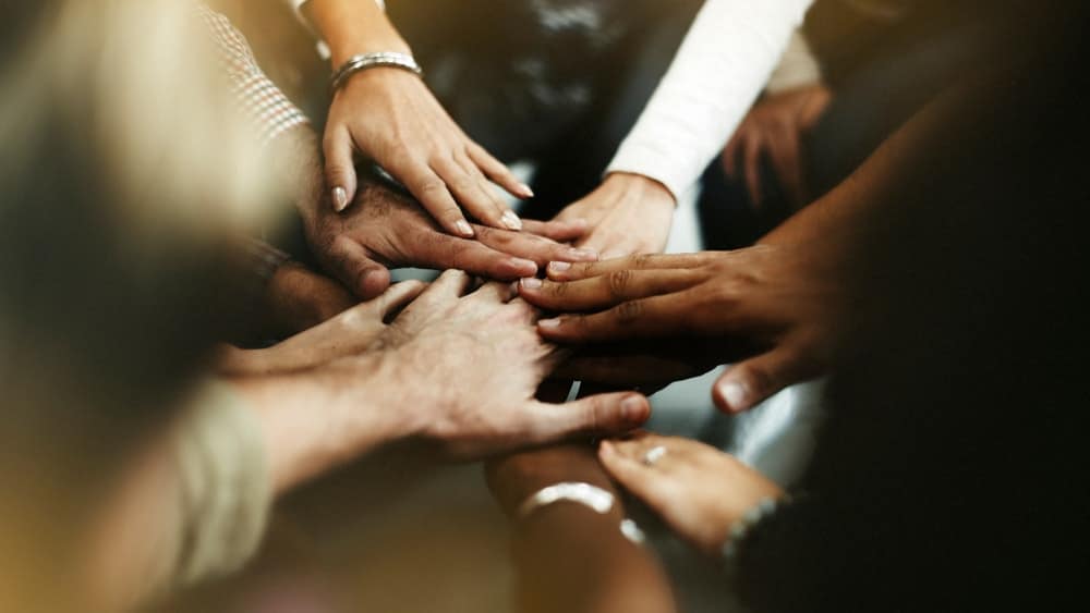 A group of people demonstrating unity by putting their hands together in a circle.