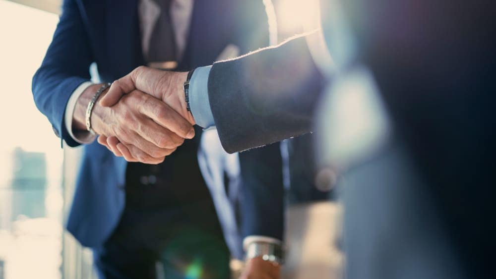 Two businessmen from a private company shaking hands in front of a window, possibly discussing public-private partnerships or Manitoba leases park.