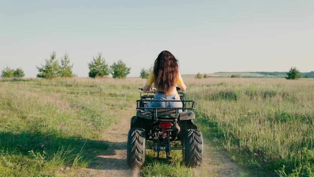A girl joyfully riding an ATV in a vast field.