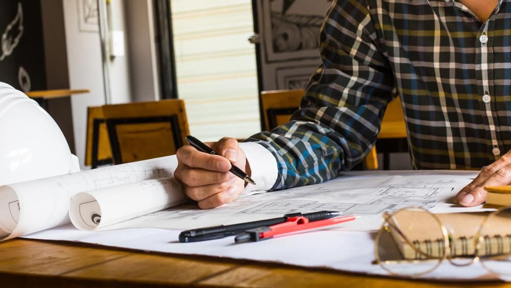 A man is working on blueprints at a table.