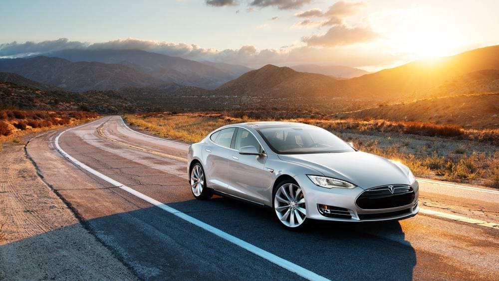 The Tesla Model S, an electric vehicle, is driving down the road at sunset.