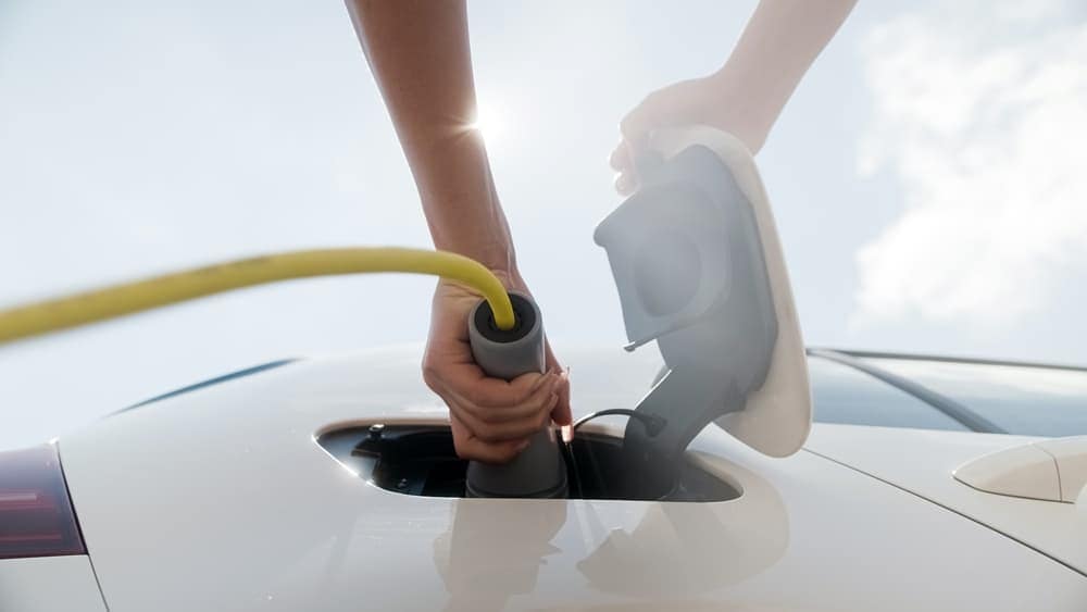A person is charging a car with a yellow cord as part of the Canadian Gov't's EV charger investment.