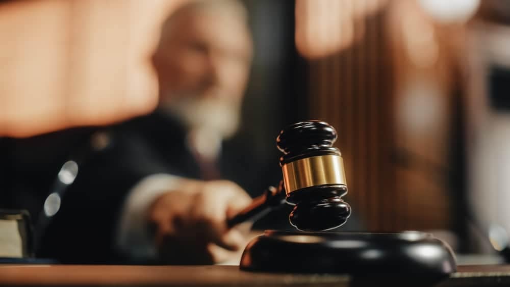 A judge in a courtroom is holding a gavel as he presides over a Senate Committee hearing concerning an Outdoor Recreation bill.