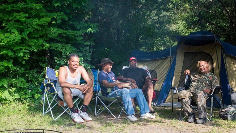 A group of people sitting in lawn chairs near a tent at Pinckney Recreation Area.