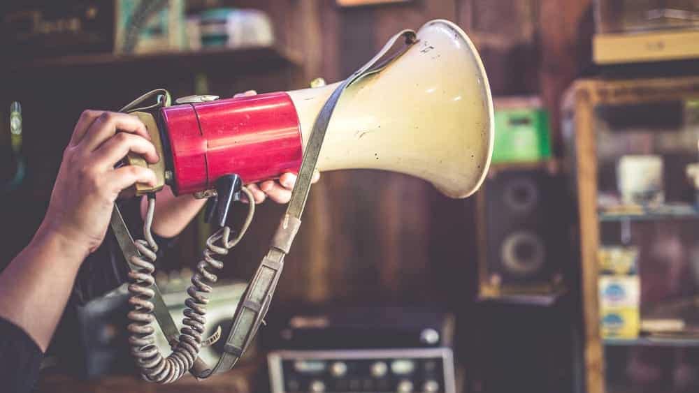 A person holding a megaphone advocating for National Park Visitor Reservation System Reform in a room.