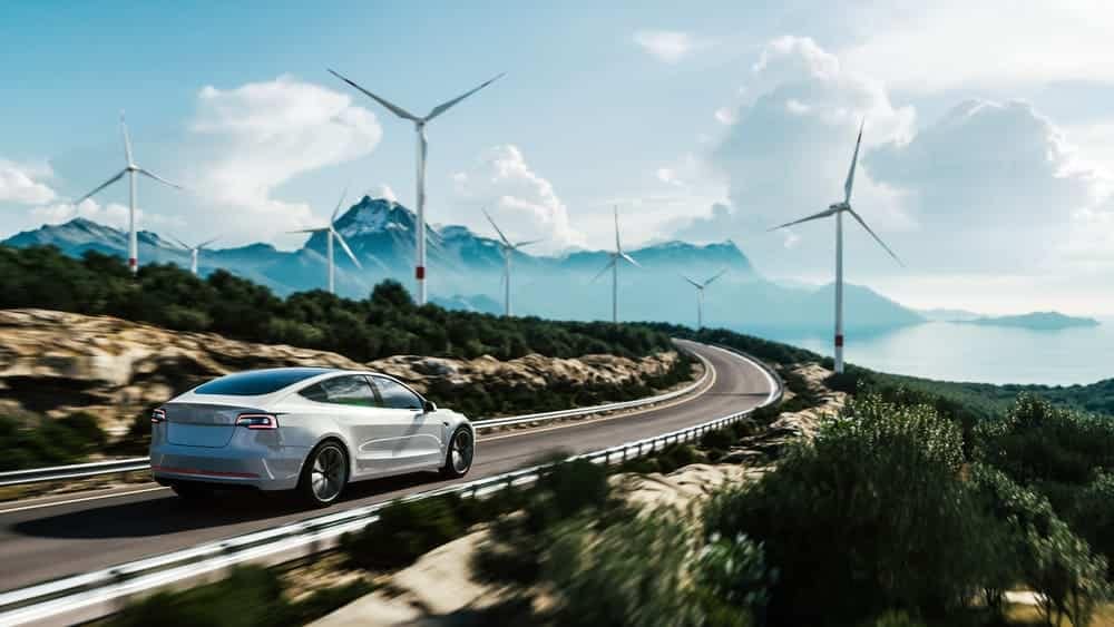 An electric car driving down a road with wind turbines in the background.