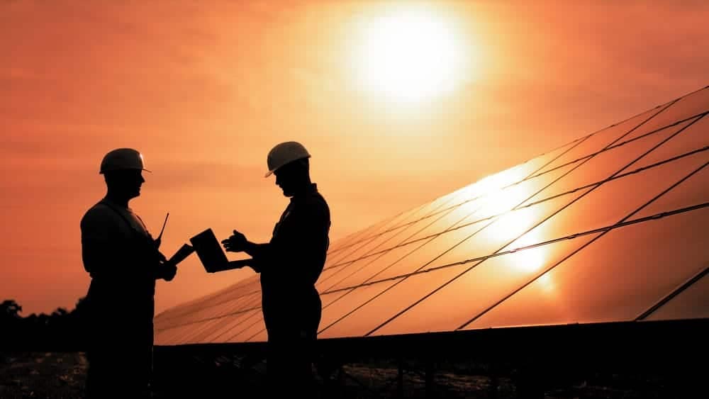Two men in hard hats standing in front of a solar panel at the Foreshore Caravan Park.