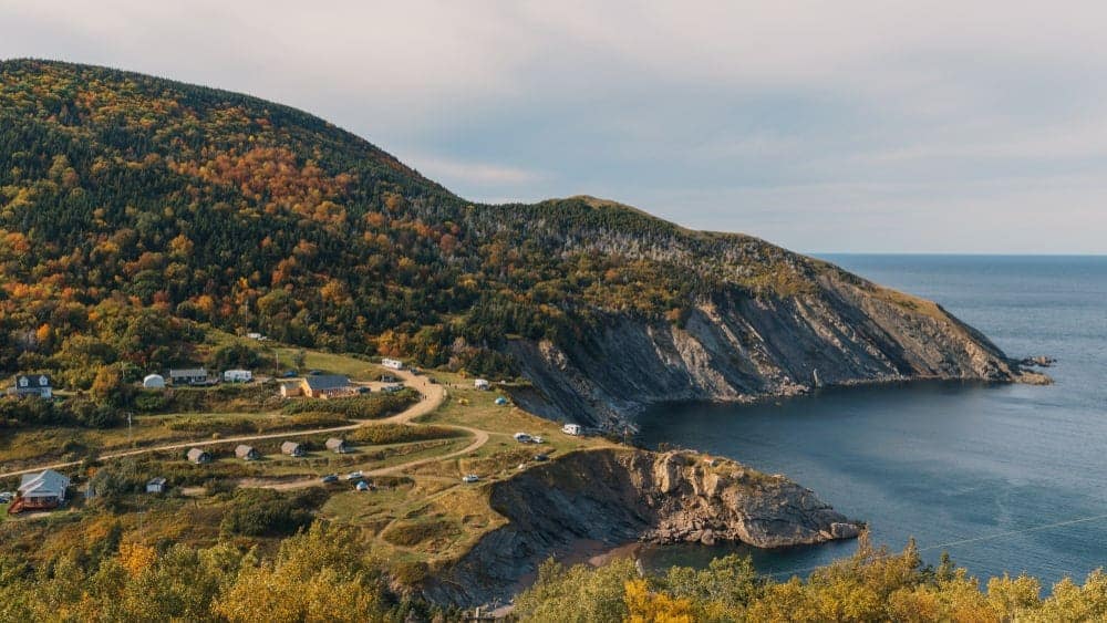 A breathtaking view of a cliff overlooking the majestic ocean and a picturesque village nestled in Eastern Nova Scotia.
