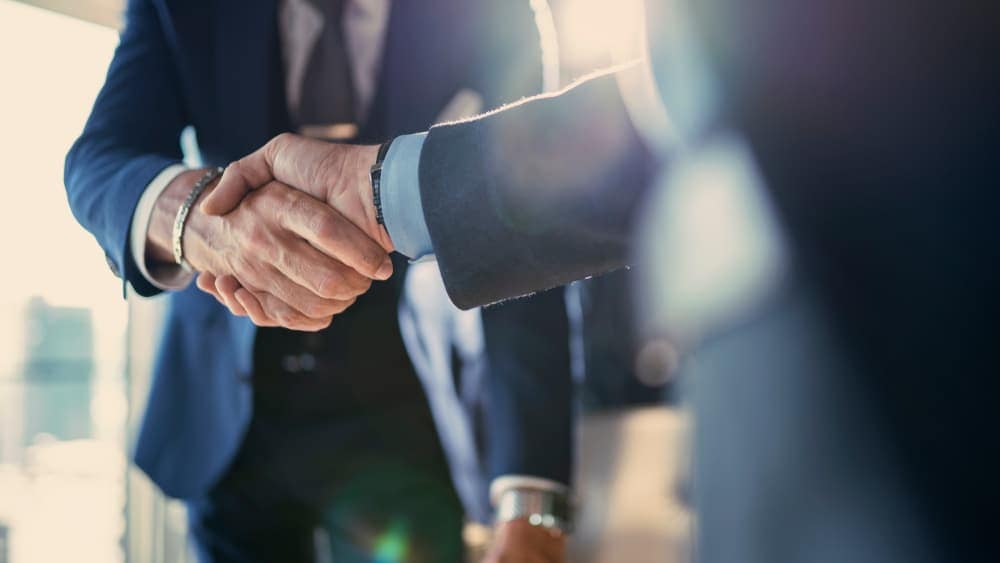 Two businessmen shaking hands in front of a window, demonstrating a Thor-like electrification in their collaboration - a harbinger of success.