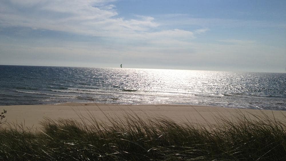 Muskegon State Park is a beautiful sand beach with a sailboat gracefully sailing in the water.