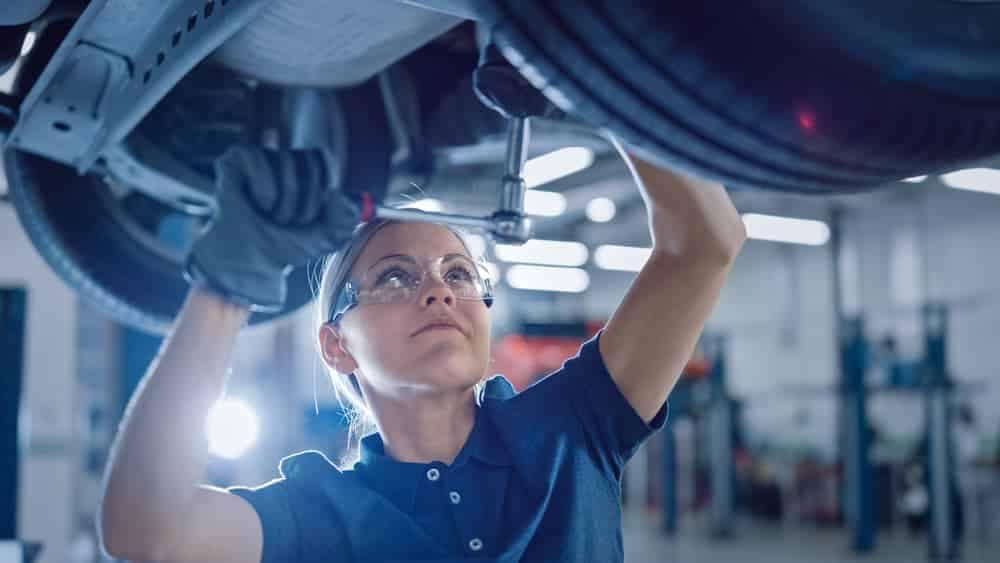 An empowered woman working on a car in a garage, showcasing her skills and expertise obtained through technician training courses.