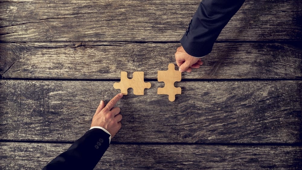 Two business people holding a piece of jigsaw puzzle on a wooden table during an acquisition meeting at a campground.