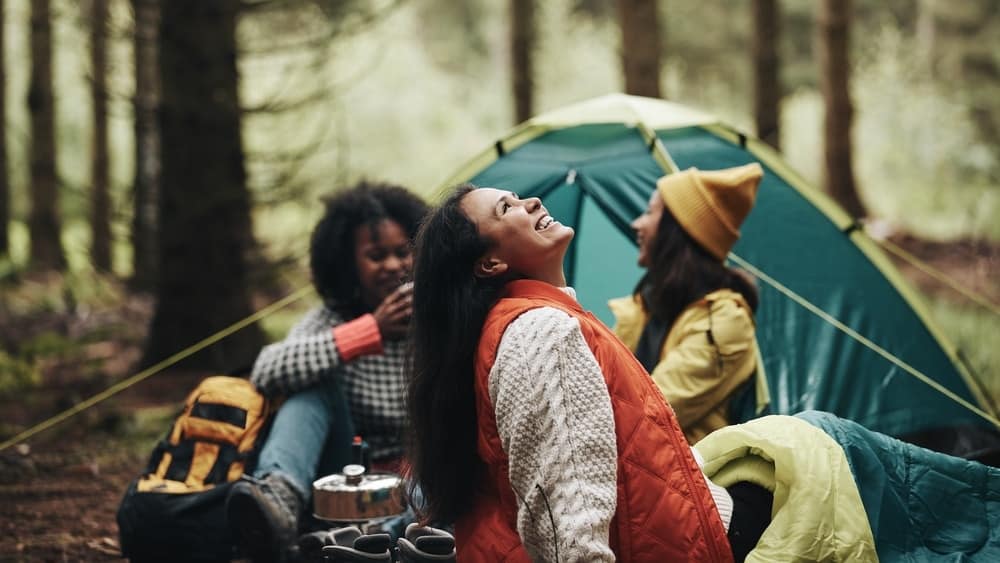 A group of women sitting in front of a tent in the woods, enjoying their culturally conscious camping experience at Spacious Skies Campgrounds.