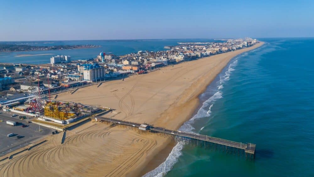 Aerial view of a sandy beach with a pier extending into the ocean, surrounded by a coastal city under a clear blue sky, featuring an Auto Draft.