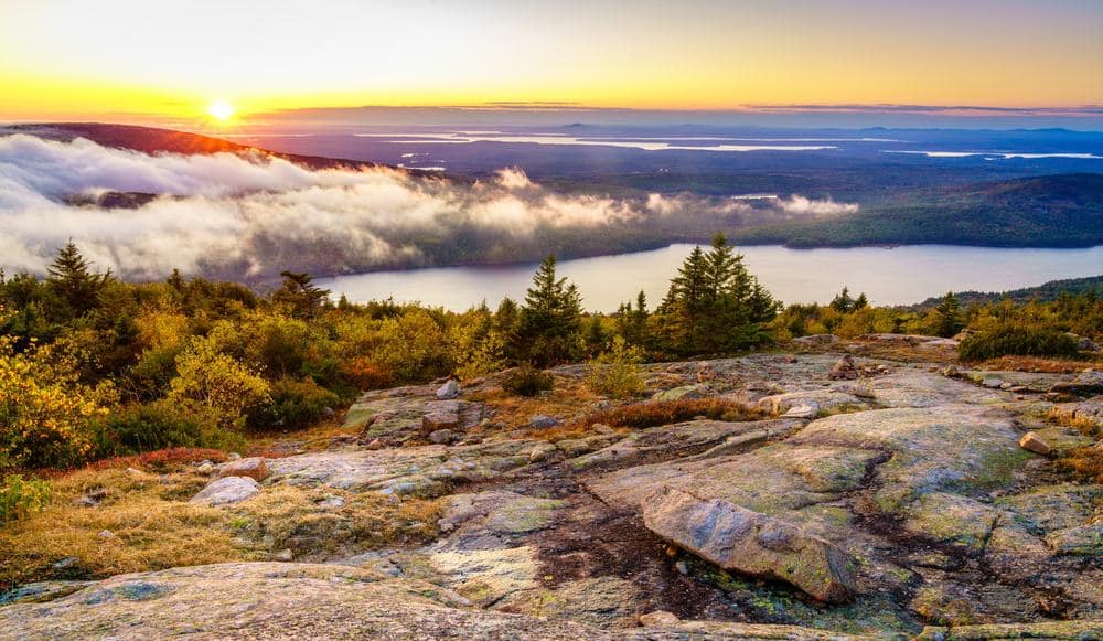 The sun rises over a lake and mountains in Acadia National Park.