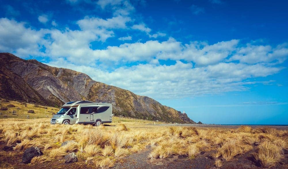 A Knaus-Tabbert Pop-Top Motorhome parked in a grassy field near the ocean.