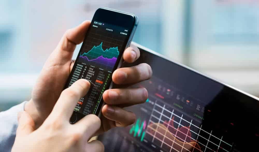 A person holding a smart phone with a preliminary stock chart on it.