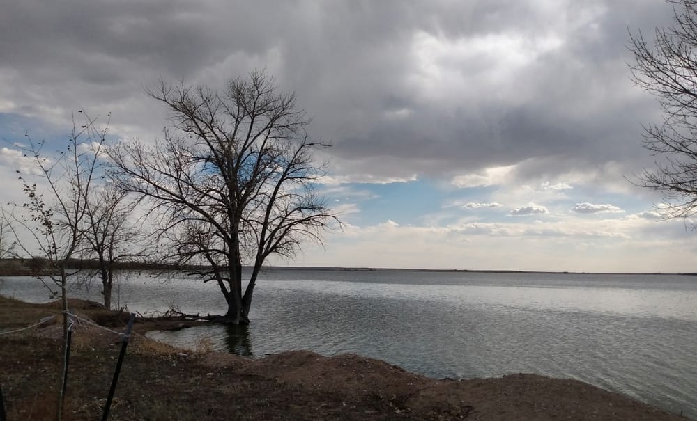 A serene lake surrounded by lush trees and under a cloudy sky at Julesburg Reservoir State Wildlife Area.