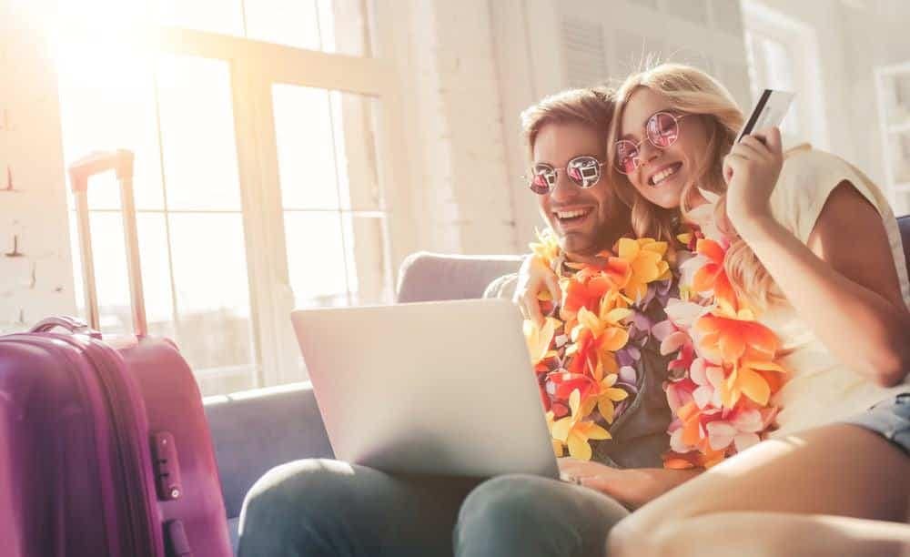 Two Americans sitting on a couch and using a laptop to check their Tripadvisor reviews before spending on their upcoming trip.