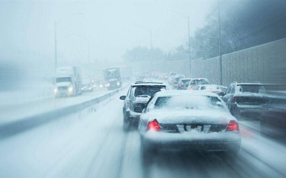 A snowy highway with cars driving in a winter storm.