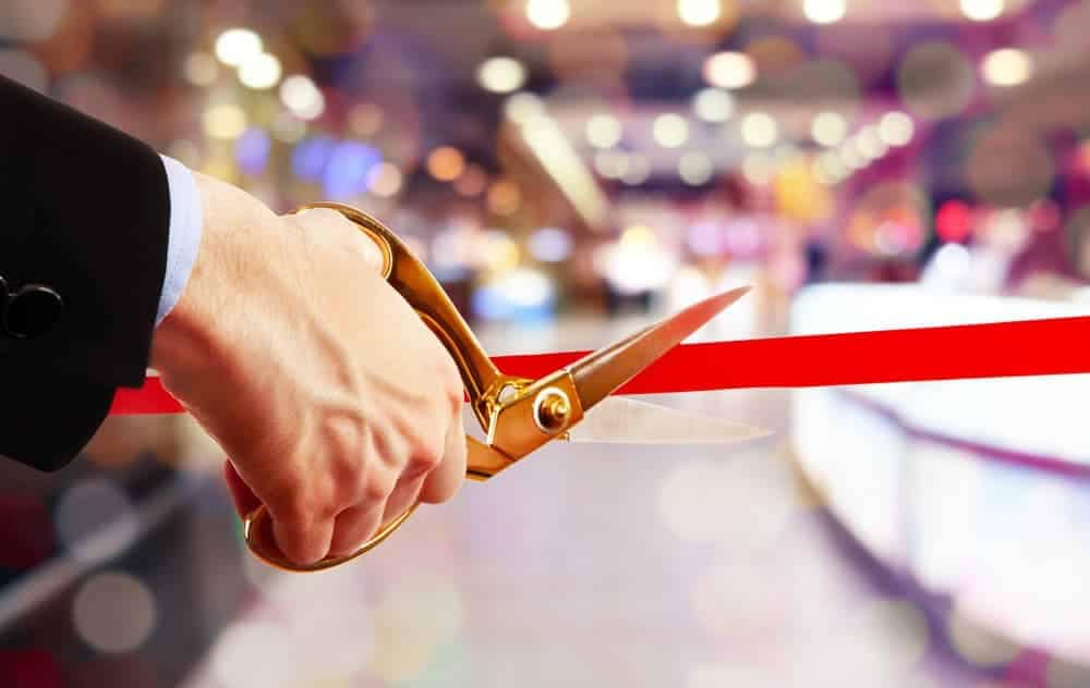 A man performing the grand opening ceremony by cutting a red ribbon in front of a crowd at Carefree Covered RV storage.