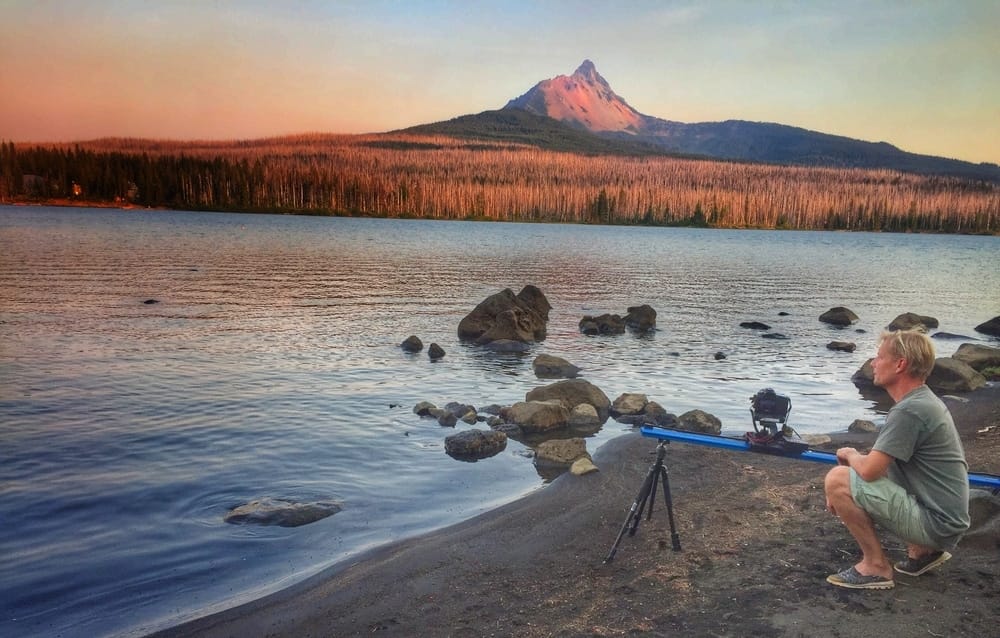 A man capturing the prime viewing experience of an annular eclipse at a lake with a tripod.