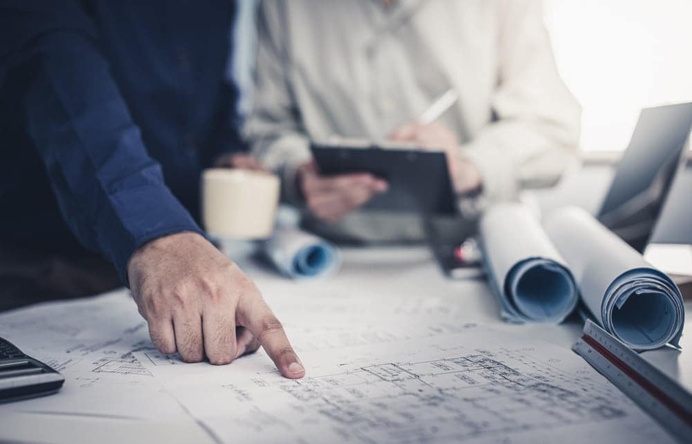A man and woman are working on blueprints for a proposal in an office.