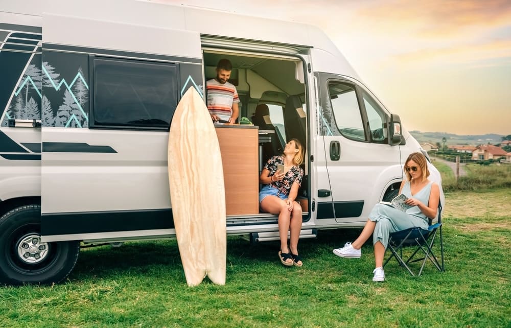 A group of people sitting in front of a camper van with surfboards.