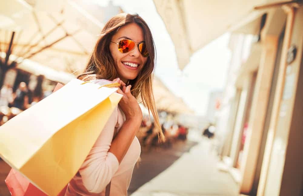 A woman wearing sunglasses and holding shopping bags on a European street, enjoying the hot summer deals.