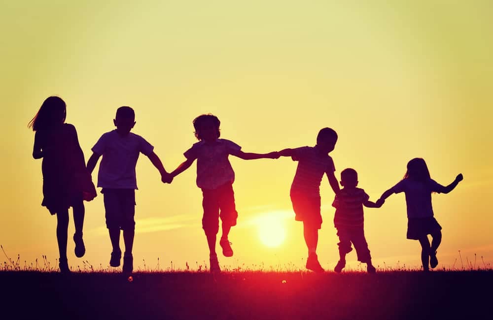 Silhouettes of a group of children running at sunset to raise money for Care Camps, supporting kids with cancer.