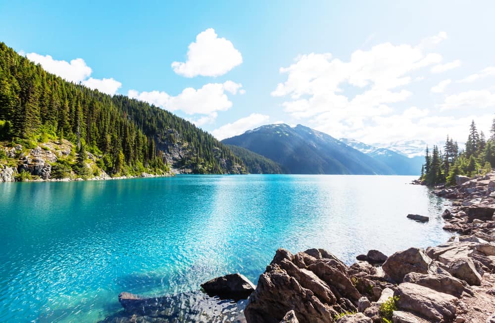 An outdoor recreation hotspot in B.C., the blue lake is set amidst rocks and trees, attracting visitors during the busy summer season.