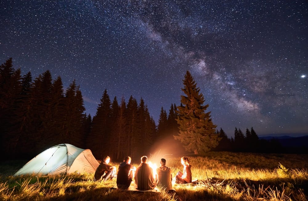 A group of people sitting around a campfire under the stars.