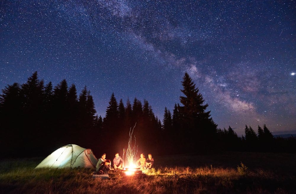 A group of people sitting around a campfire under a starry sky during the Camping Season.