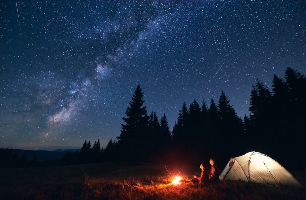 A person is camping under a starry sky at Louisiana State Parks with a tent in the background, enjoying overnight stays.